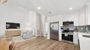 A modern kitchen with white cabinets, stainless steel appliances, and a wooden floor.