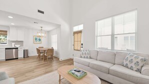 A spacious living room with a sofa, a dining table, and a kitchen in the background.