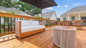 A wooden deck with a white sofa, wicker chairs, and a round table.