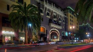 A hotel with a prominent archway entrance, palm trees, and a well-lit street with light trails. - Santana Row Properties #9 - Silicon Valley Getaway: Escape the Ordinary! (San Jose)