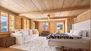 Een gezellig houten kamer met een bank, een bed en een groot raam met uitzicht op de bergen.