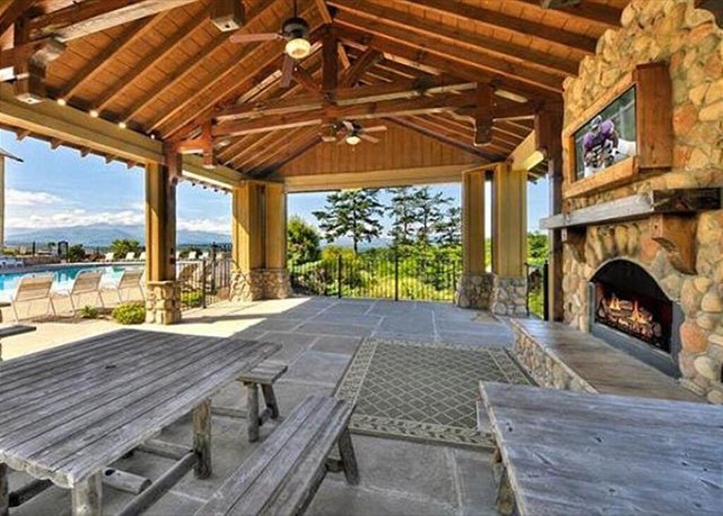 An outdoor patio with stone walls, a fireplace, and a pool in the background.