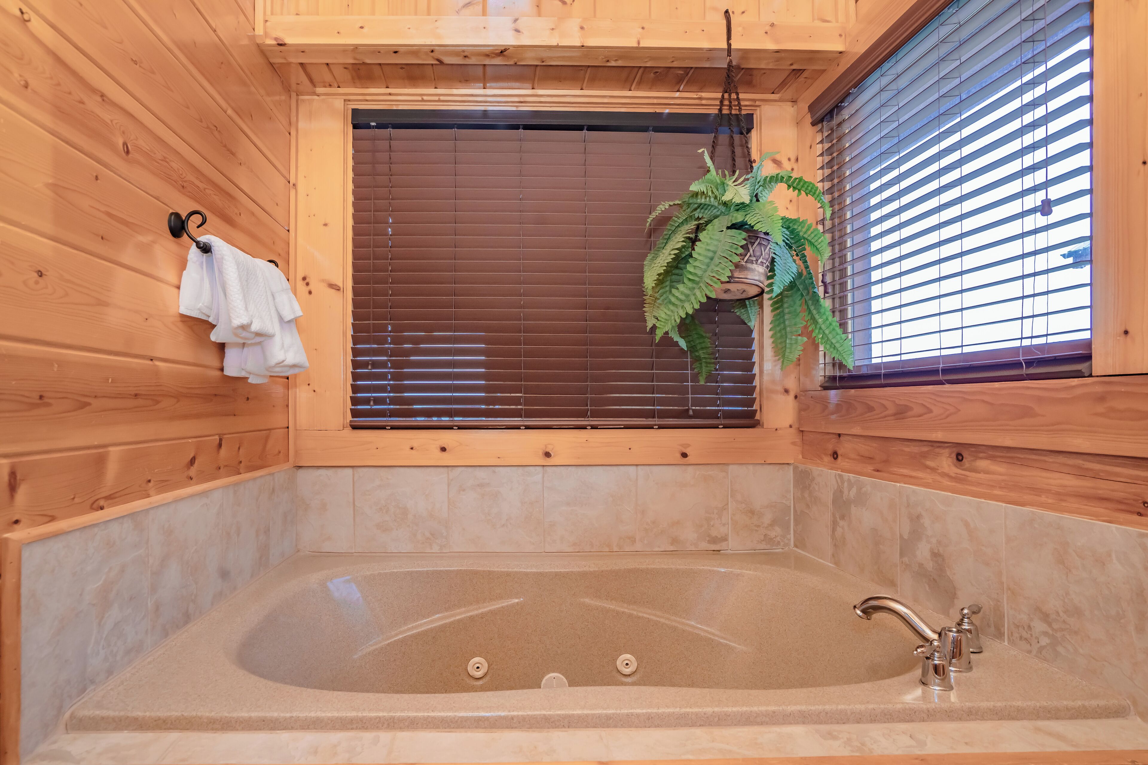 Une cabane en bois avec une grande baignoire, des murs en bois, une fenêtre avec des stores et une plante suspendue.