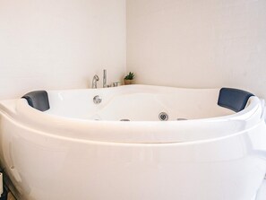 A large, white, freestanding bathtub with a single faucet and a small potted plant beside it.