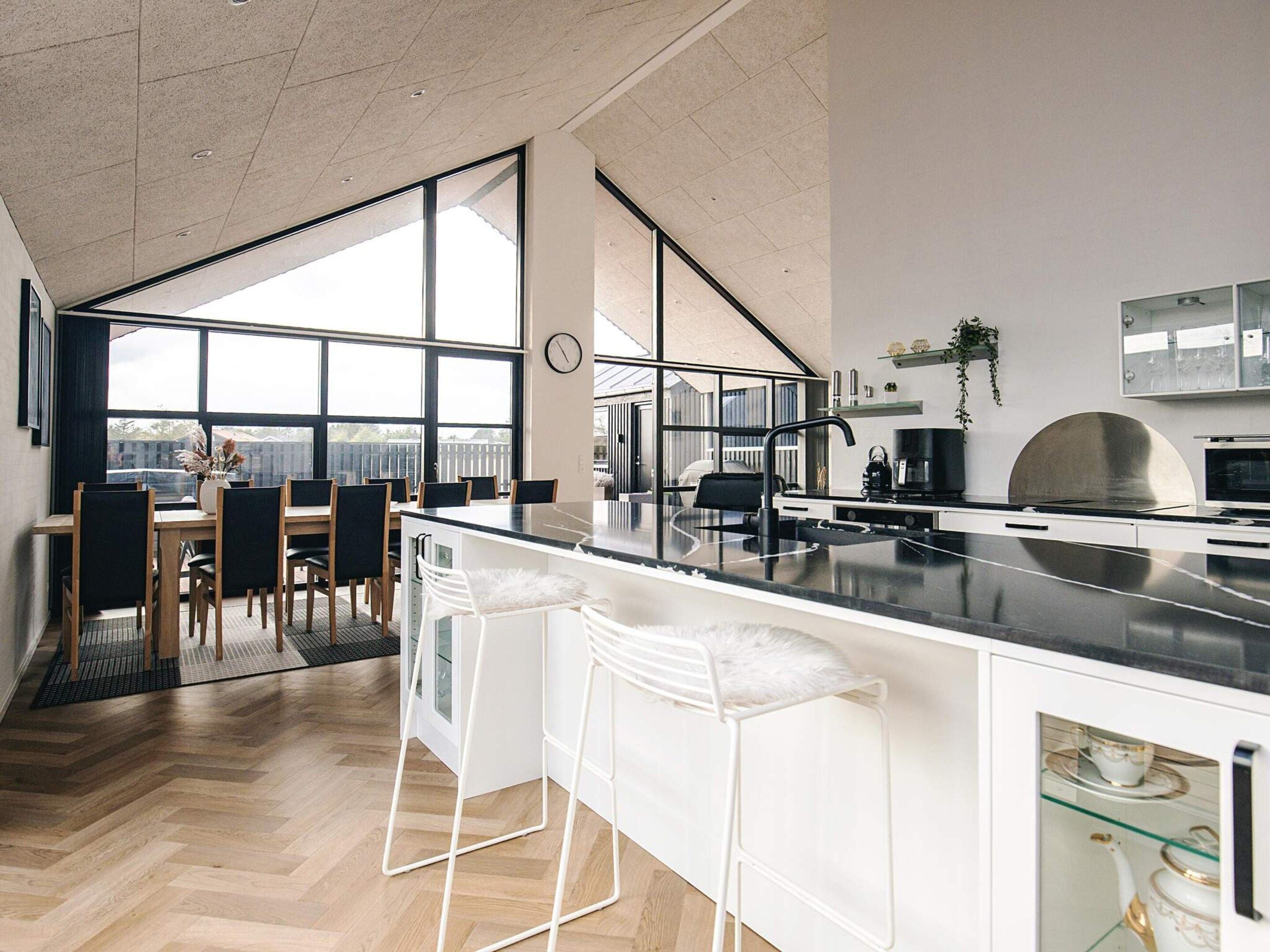 A modern kitchen with a large island, bar stools, and a dining area with a view.