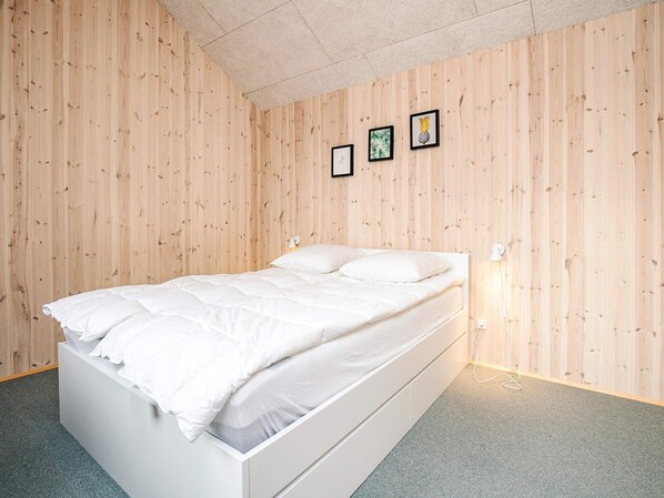 A bedroom with a white bed, wooden walls, and three framed pictures on the wall. - 5 Star Holiday Home in Lokken (Lokken)