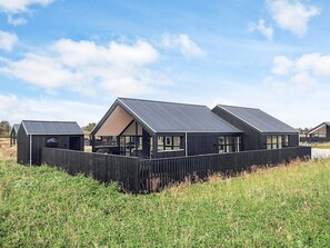 A row of modern, dark-colored cabins with large windows, set in a grassy field with a clear sky. - 5 Star Holiday Home in Lokken (Lokken)