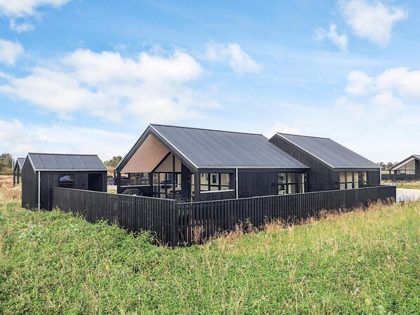 A row of modern, dark-colored cabins with large windows, set in a grassy field with a clear sky.