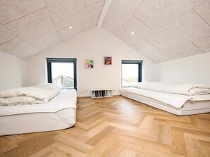 A spacious attic bedroom with two beds, wooden flooring, and large windows. - 5 Star Holiday Home in Lokken (Lokken)