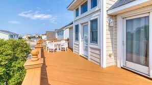 A wooden deck with outdoor furniture, a glass door, and a view of neighboring houses. - 3 BUOYS, 1 GULL - 5-bedroom house within walking distance to beach access (Kill Devil Hills)