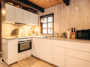 A modern kitchen with white cabinetry, a built-in oven, a microwave, and a window providing natural light.