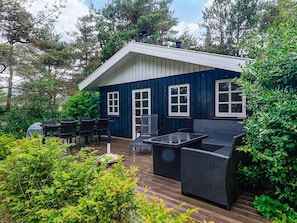 A blue house with a deck, outdoor furniture, and surrounding greenery.