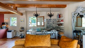 A cozy room with a sofa, a dining table, and a kitchen area with a stone wall and wooden beams.