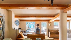 A cozy living room with a wooden ceiling, a sofa, a dining table with glassware, and a view of the outside.