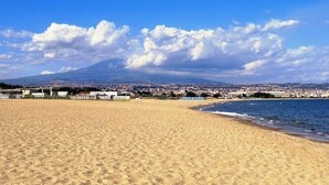 Una playa con una montaña al fondo, cielos despejados y un paisaje urbano al otro lado del agua.