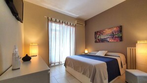 Una habitación de hotel con una cama, lámparas de noche, un cuadro en la pared y un escritorio con un florero.