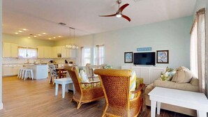 A spacious living area with a sofa, two wicker chairs, a dining table, and a kitchen in the background. - FD186 Shared Pool, Pet Friendly, Golf Cart Included, Boardwalk to the Beach (Port Aransas)