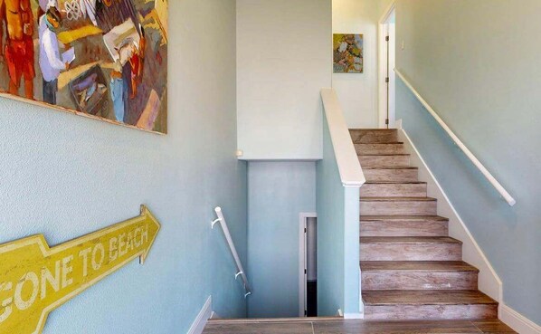 A staircase with wooden steps and white handrails, a wall-mounted sign reading "GONE TO BEACH", and a colorful abstract painting above the stairs.