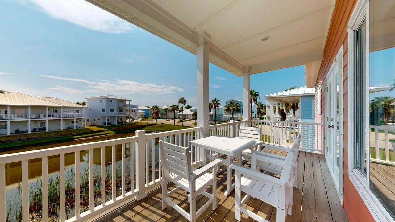 A covered outdoor area with white furniture, a view of a beach, and a building with a white facade.