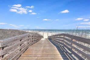 A wooden boardwalk leading to a beach with a clear sky.