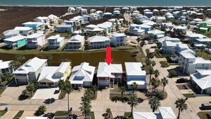 An aerial view of a coastal residential area with houses arranged in rows, a body of water in the foreground, and a beach visible in the distance. - FD186 Shared Pool, Pet Friendly, Golf Cart Included, Boardwalk to the Beach (Port Aransas)