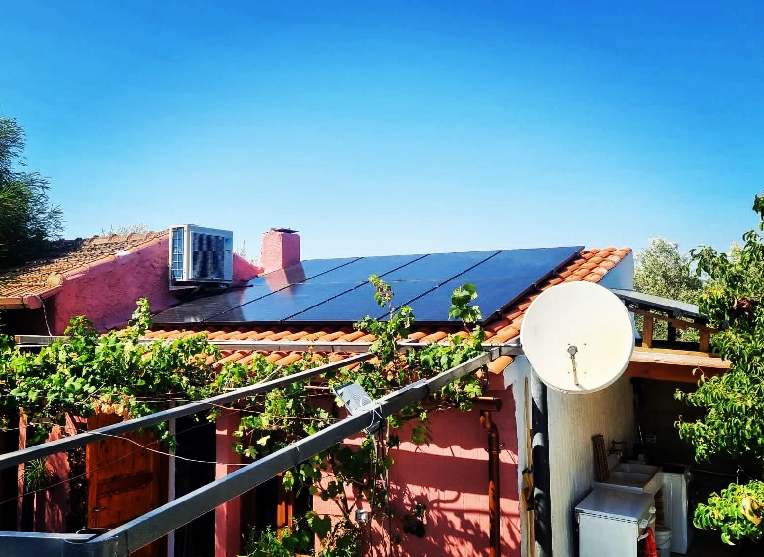 A rooftop with solar panels, a satellite dish, and a red building with a chimney.