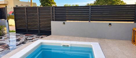 Una piscina con un borde de baldosas y una valla negra al fondo.