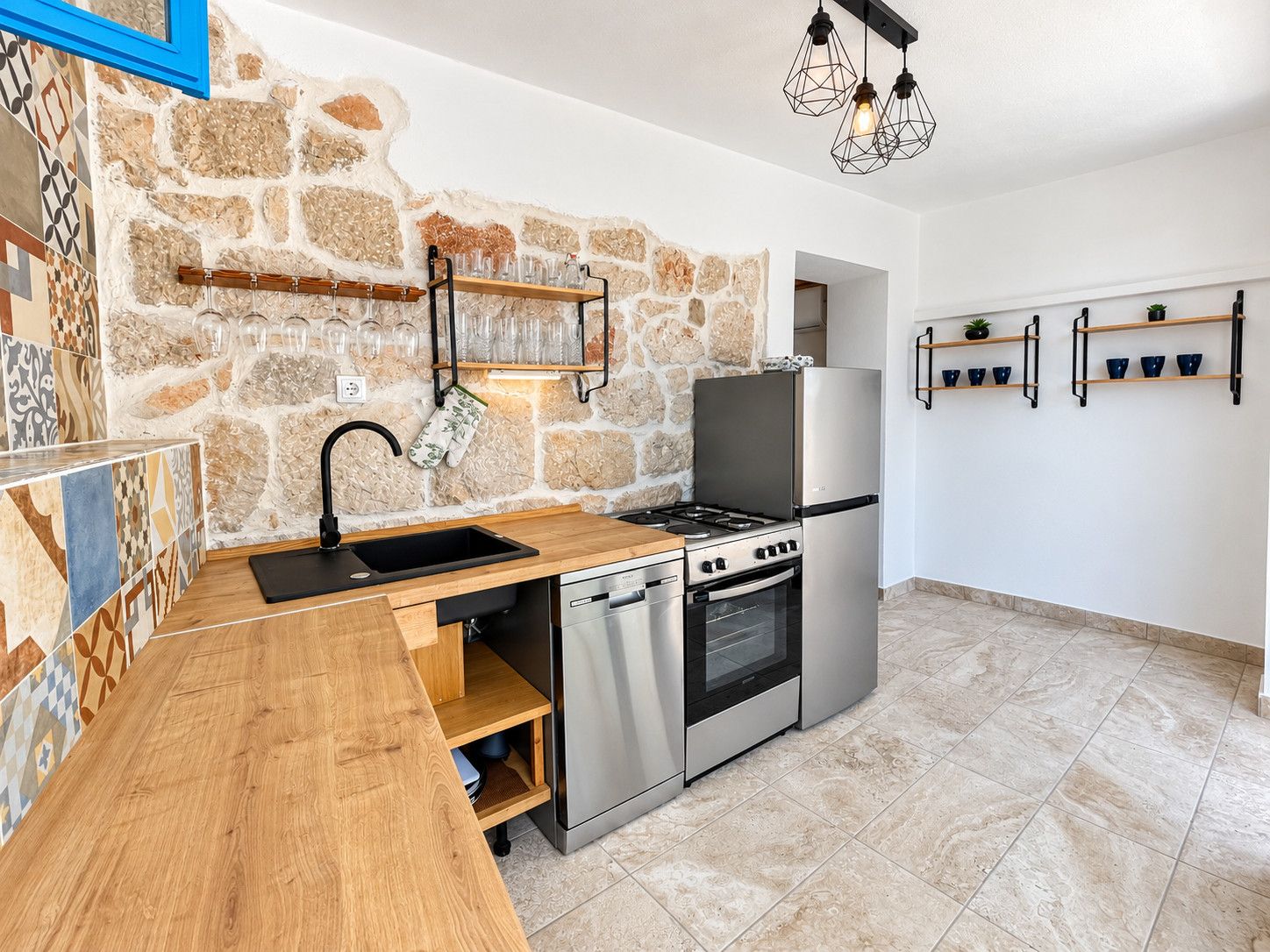 A compact kitchen with a stone wall, stainless steel appliances, and a wooden countertop.