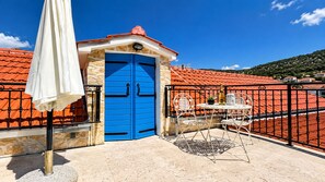 Un balcon avec une porte bleue, un parasol blanc et une table avec des chaises.