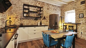 A rustic kitchen with stone walls, wooden beams, and a dining area with blue chairs. - Holiday Home Tranquilla with heated pool (Blato)