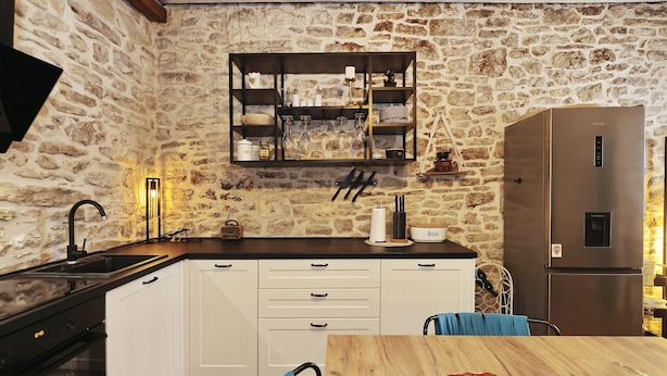 A rustic kitchen with a stone wall, a wooden shelf with glassware, a stainless steel refrigerator, and a wooden dining table. - Holiday Home Tranquilla with heated pool (Blato)