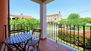 Un balcon avec une table et des chaises en bois, un sol carrelé et une vue sur un jardin et des bâtiments en arrière-plan.