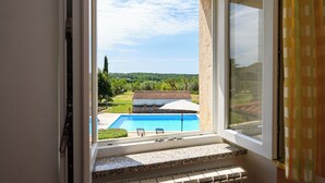 Une fenêtre donnant sur une piscine, un toit recouvert de tuiles et un paysage verdoyant.