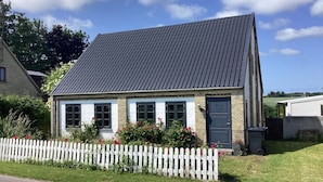 Una casa de dos pisos amb un teulat fosc, parets exteriors blanques i una valla de palets blanca.