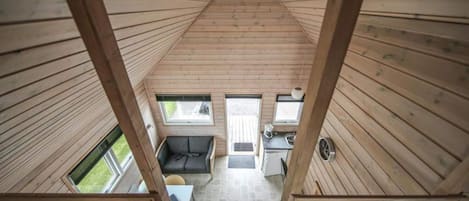 Interior de madera con techos altos, que incluye un comedor, un sofá y una cocina visible a través de las ventanas.