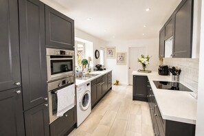 A modern kitchen with dark cabinetry, stainless steel appliances, a washing machine, and a tiled backsplash.