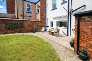 A residential property with a well-maintained lawn, a patio with a table and chairs, and a brick wall with a climbing plant.