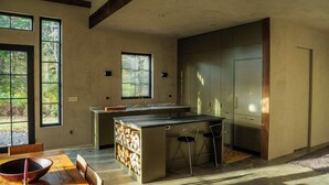 Una cocina moderna con una isla central, ventanas amplias y un comedor con mesa y sillas de madera.