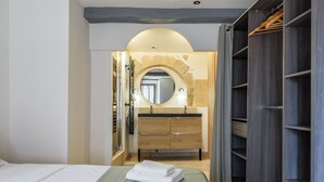 A hotel room with a bed, a vanity with a mirror, a wooden wardrobe, and a bathroom with a shower. - LA FONTAINE – Peaceful retreat in medieval Tourrettes-sur-Loup (Tourrettes-sur-Loup)