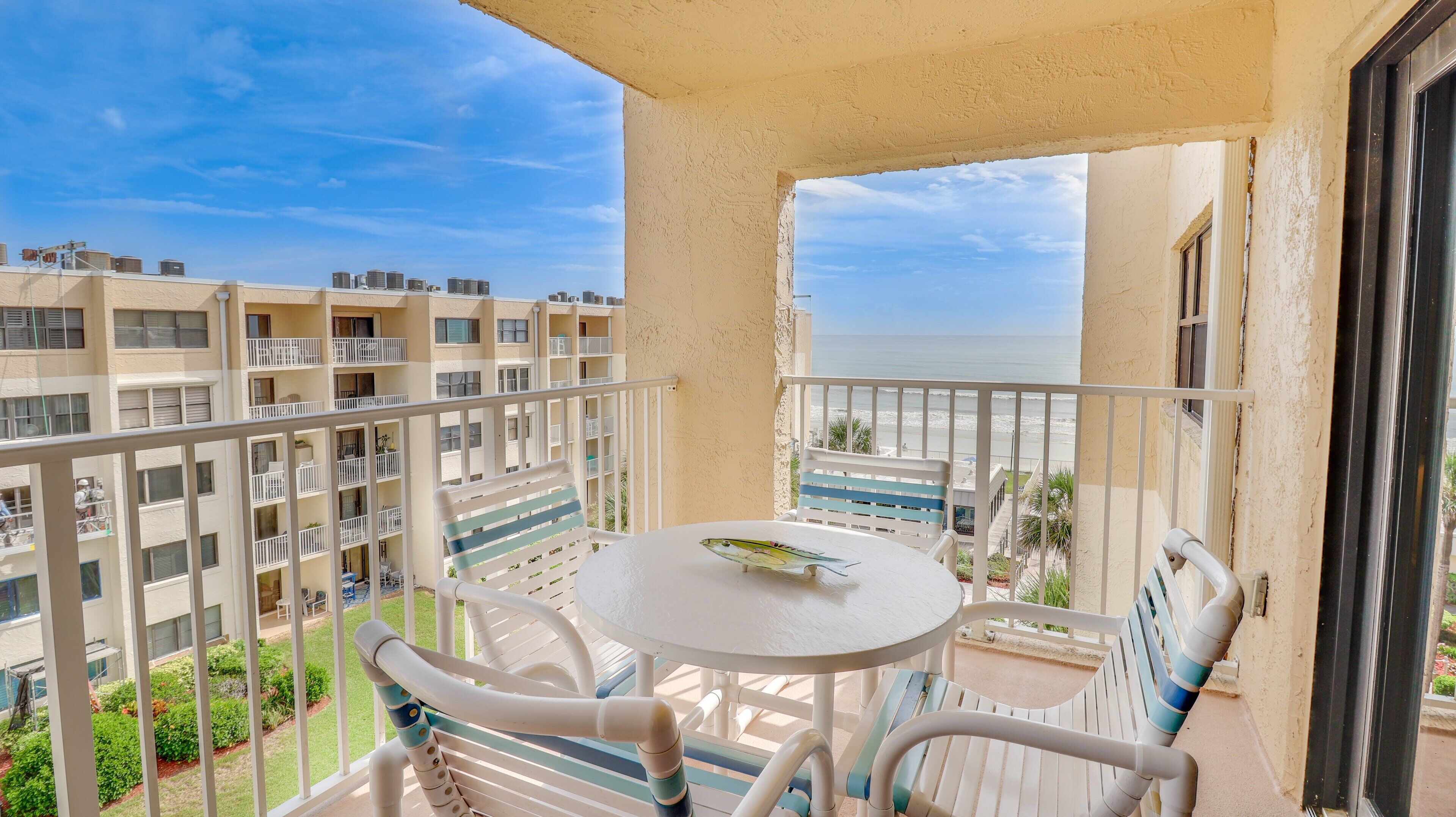 Ein Balkon mit rundem Tisch und Stühlen mit Blick auf einen Strand und angrenzende Gebäude.