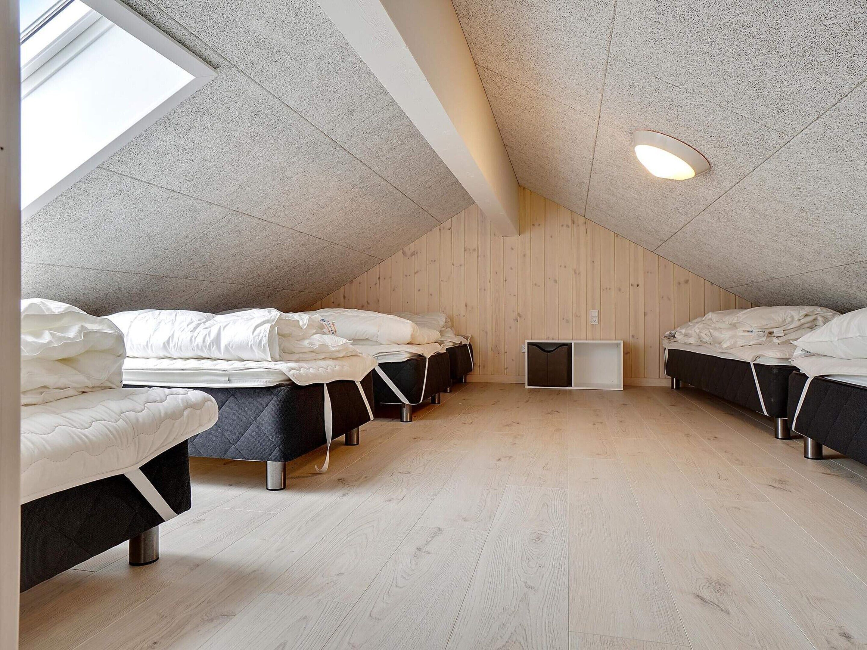 Un dormitorio con cuatro camas dispuestas en forma de U, un tragaluz y suelo de madera.