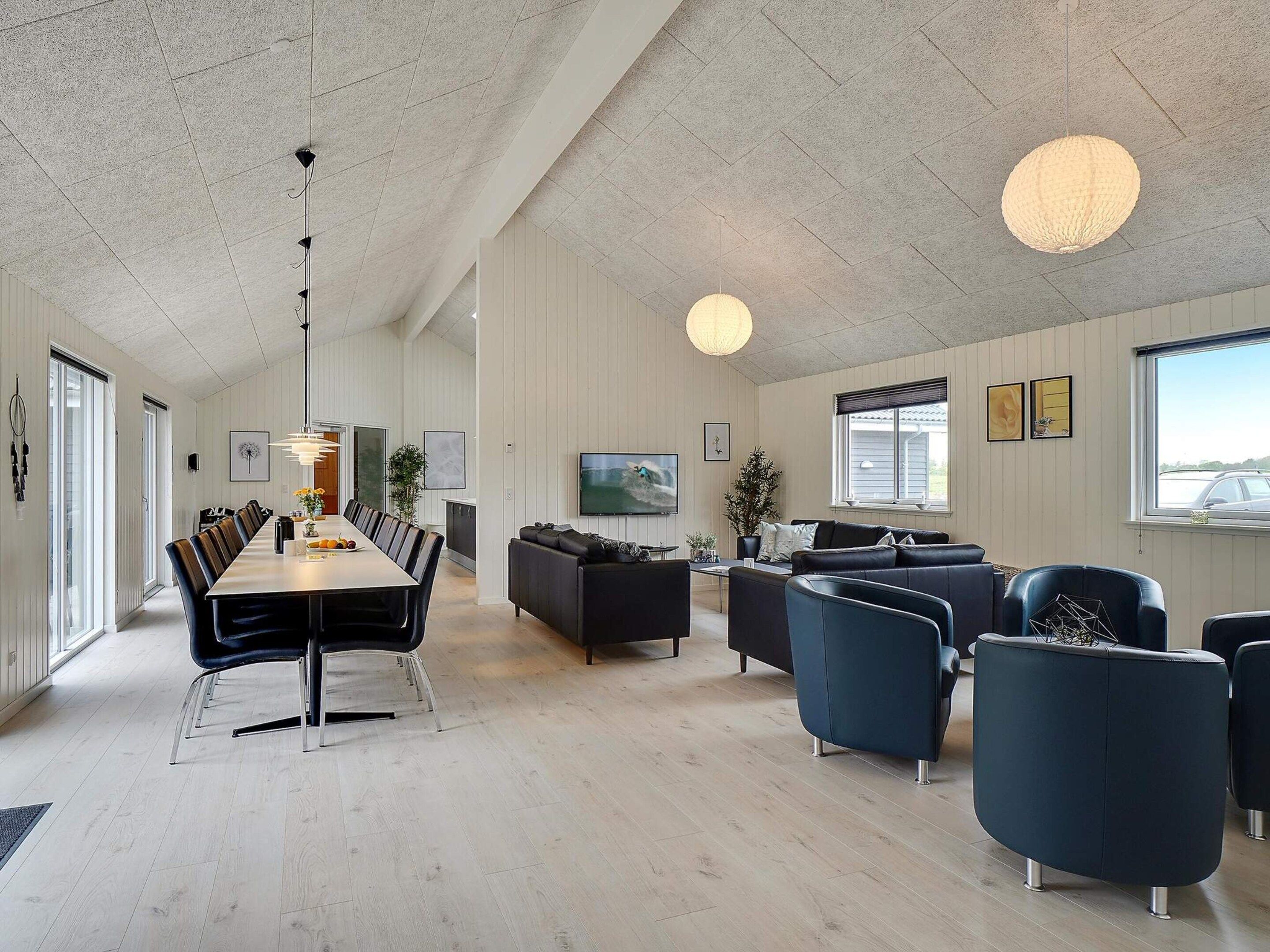 A spacious room with a long dining table, multiple chairs, a sofa, and a television.