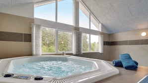 Ett bubbelbad med utsikt över träd, en handduk och en kontrollpanel.