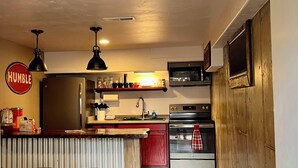 A kitchen with a refrigerator, microwave, oven, and bar stools. - Mountain View Retreat (Ennis)