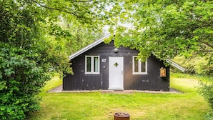 A small, dark wooden cabin with a white door and two windows, surrounded by lush greenery. - 4 Person Holiday Home in Hemmet (Hemmet)