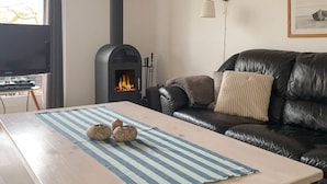 A living room with a black leather sofa, a wooden coffee table with a striped rug, a fireplace, and a television on a stand. - 4 Person Holiday Home in Hemmet (Hemmet)
