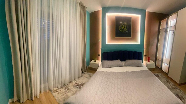 A modern hotel room with a large bed, a wall-mounted light, and a view of the city through sheer curtains. - city center 1-bedroom apartment with WiFi and AC in delightful Shkodër (Shkodër)