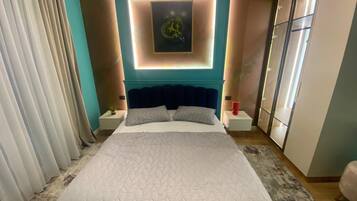 A modern bedroom with a large bed, a headboard with built-in lighting, a wall-mounted artwork, and a wardrobe with sliding doors.