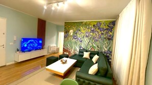 A modern living room with a green sofa, a flat-screen TV, and a floral mural on the wall. - city center 1-bedroom apartment with WiFi and AC in delightful Shkodër (Shkodër)