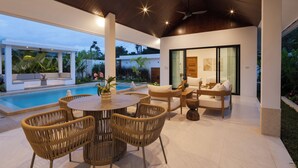 An outdoor patio with a pool, wicker furniture, and a seating area with cushions.